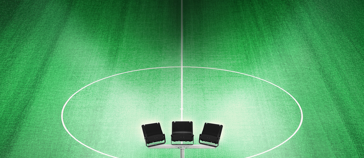 Three Ektor Commercial Floodlights mounted to a post, illuminating a grass playing field